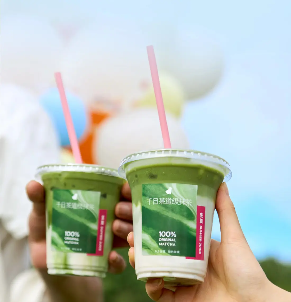 Two matcha drinks raised against the sky