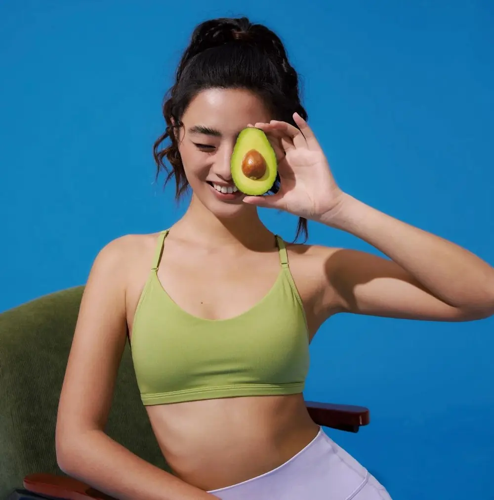Woman holding half an avocado over one eye
