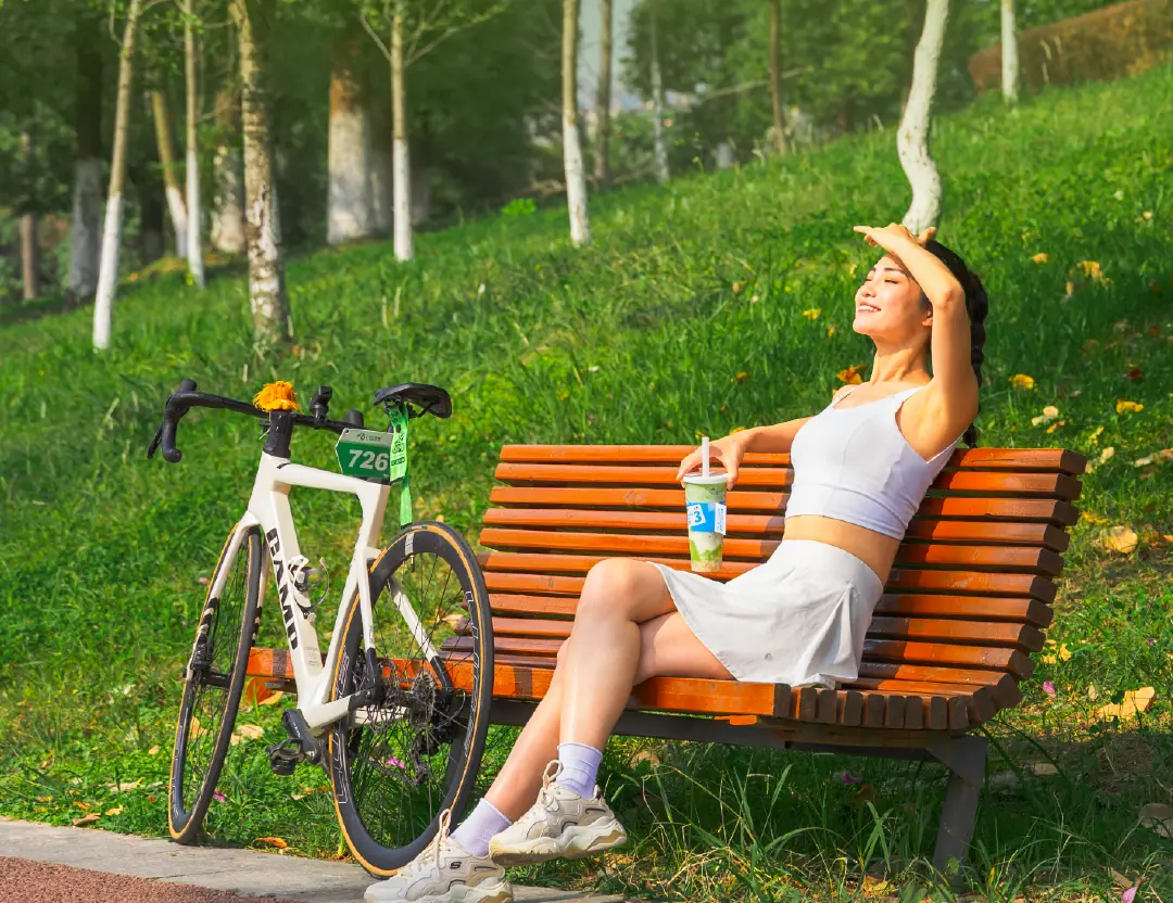 Woman resting on a park bench with a drink and a road bike